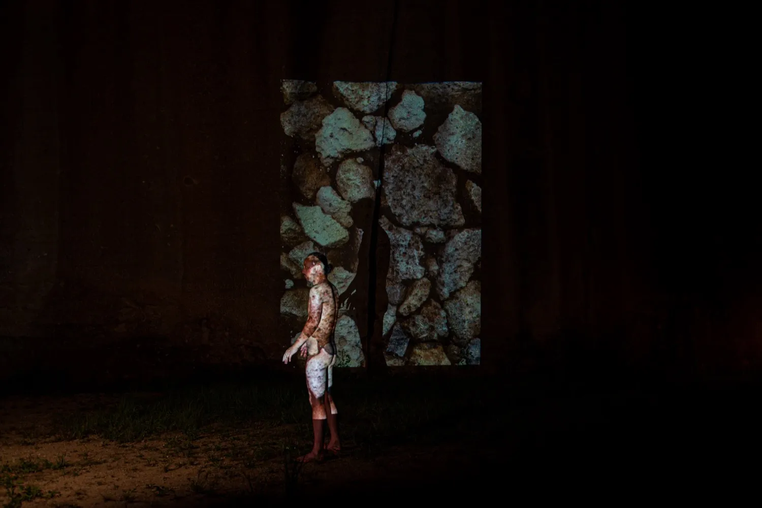 岩壁と身体に石の映像が投影された石井友人のパフォーマンス