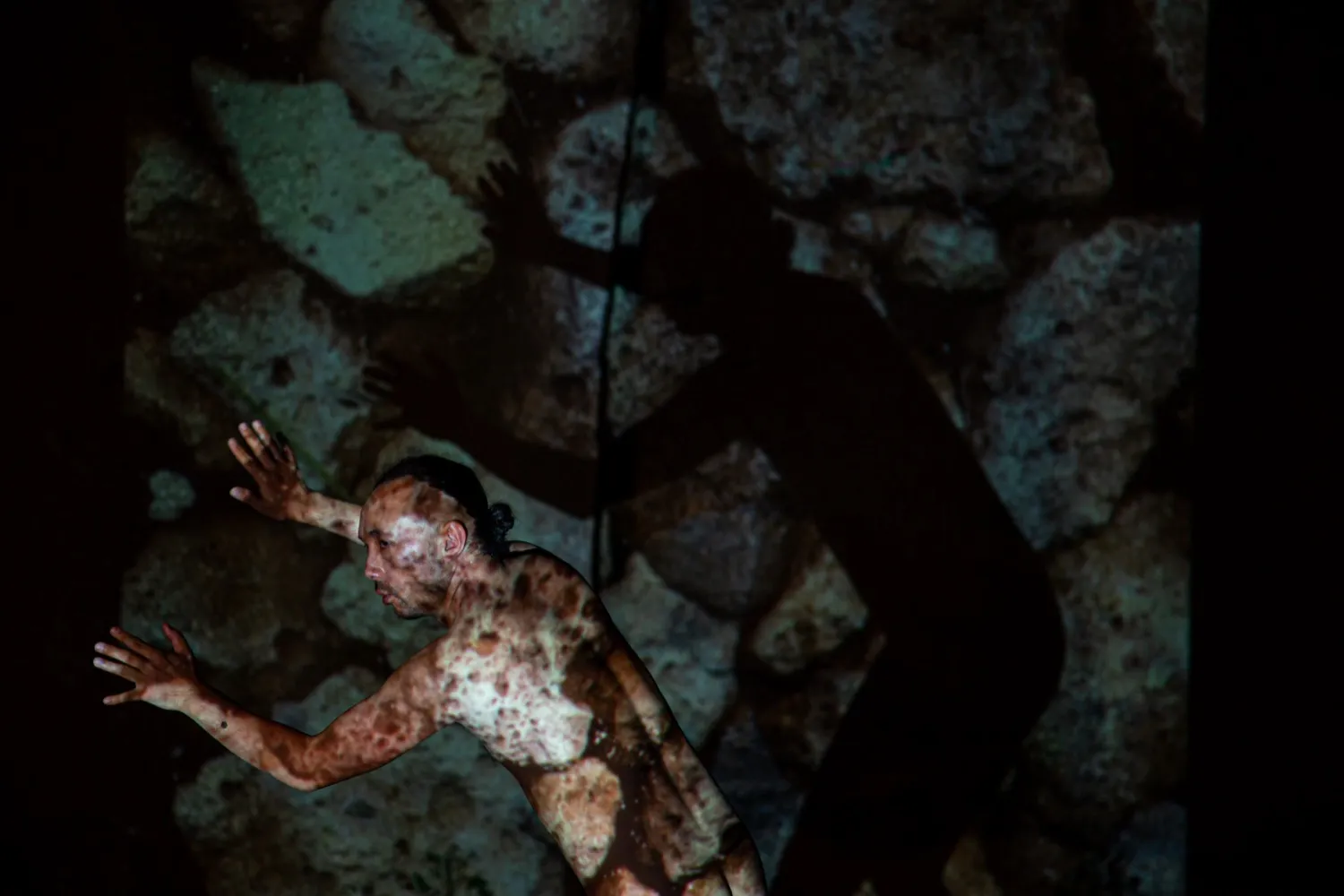 投影された岩壁の前でパフォーマンスを行う石井友人、自身の肌にも映像が投影されている