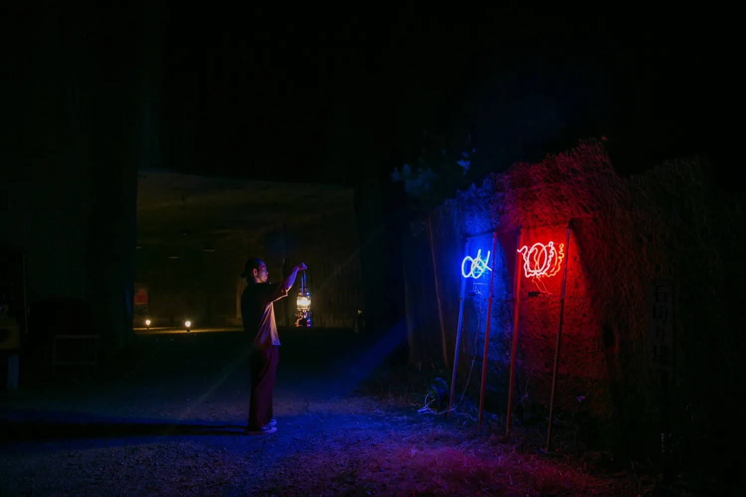 ネオンの前にランタンを持って立つ福永大介